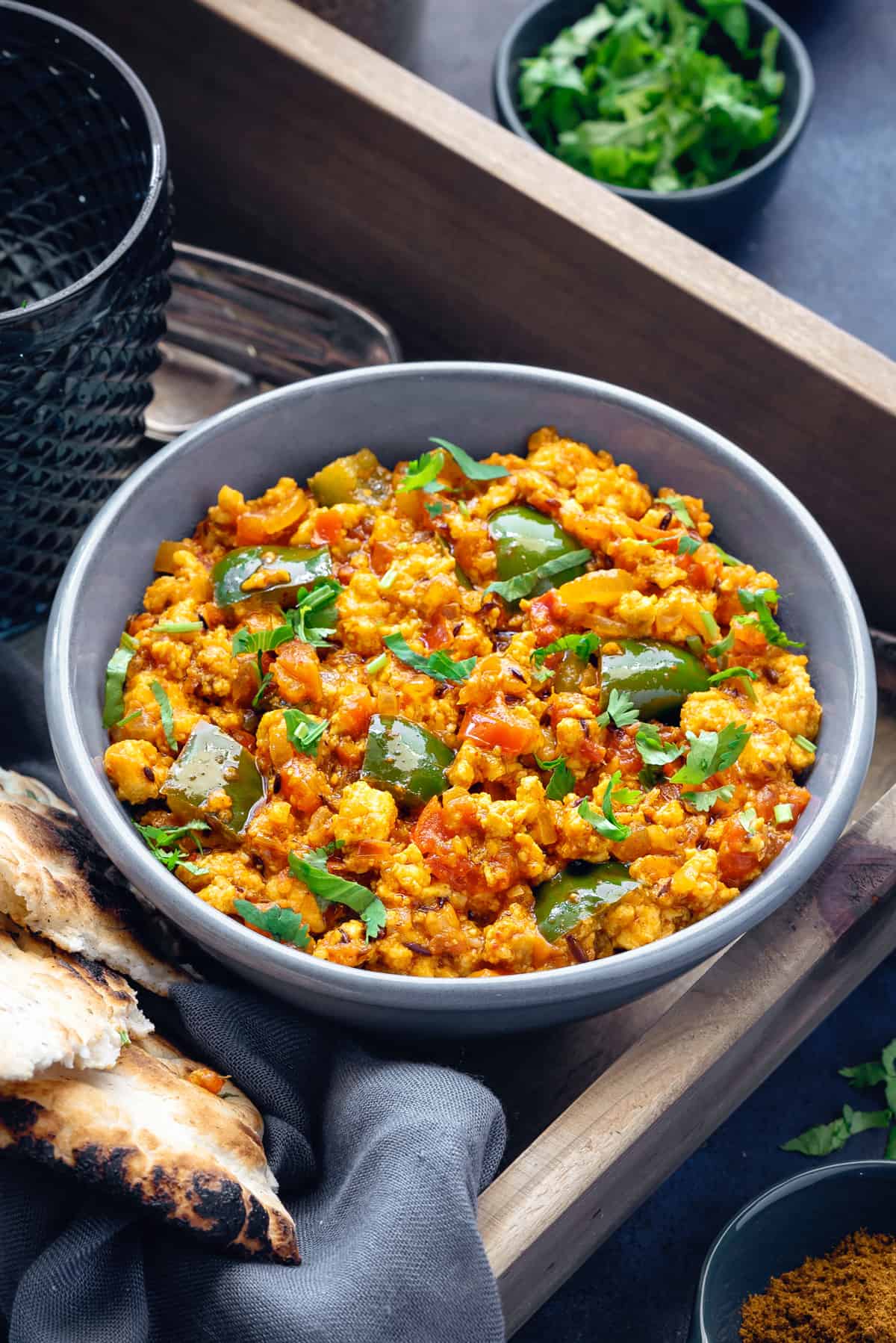 Scrambled paneer bhurji in grey ceramic bowl with naan bread on side