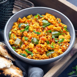 Paneer bhurji served in greay bowl with naan bread on side