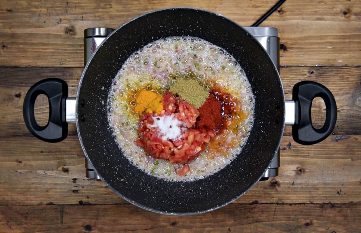 chopped tomatoes, spice powders and salt added to cooked onions in pan