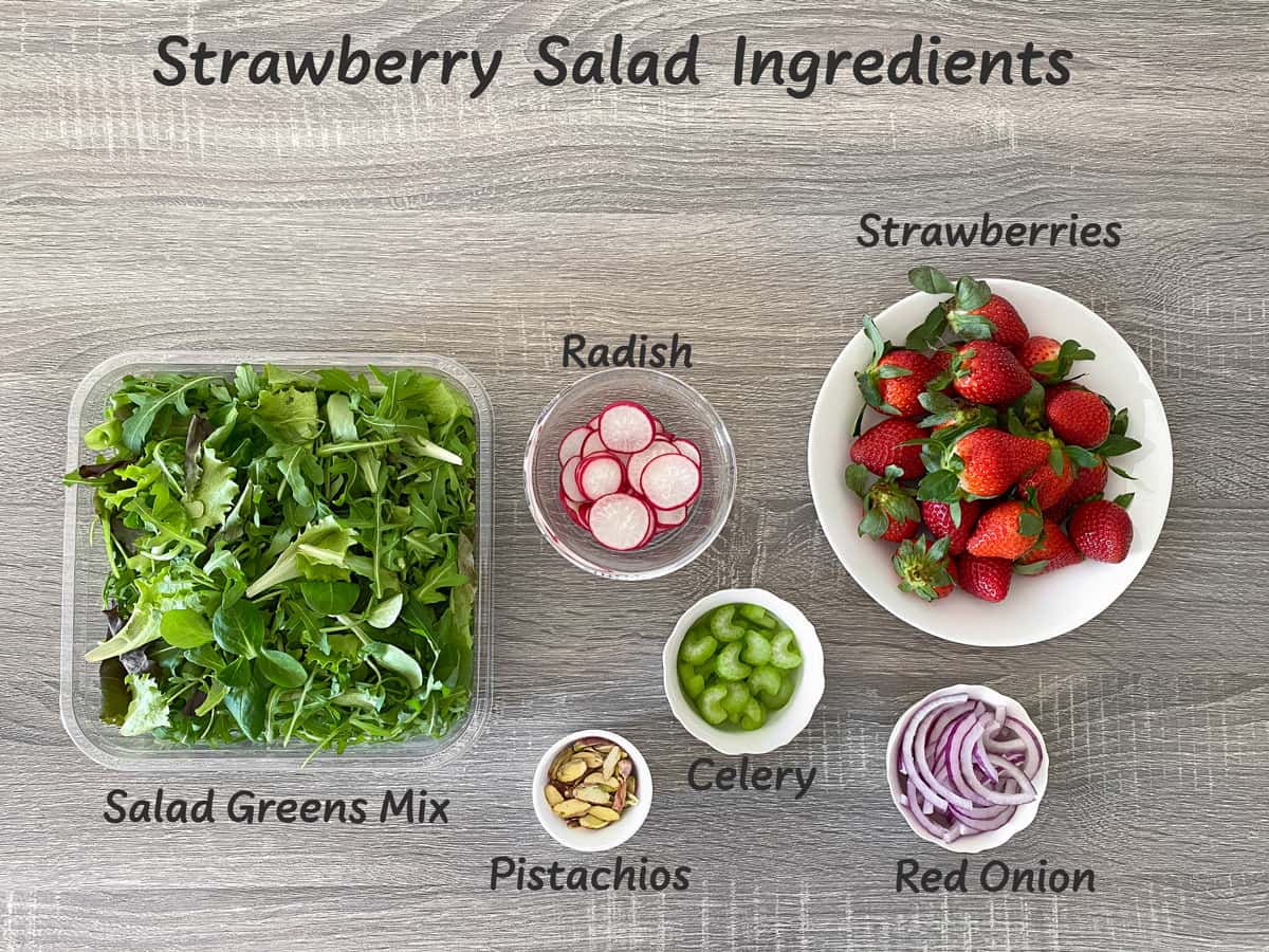 salad greens, radish, red onion, celery, shelled pistachios and fresh strawberries laid out for making a salad