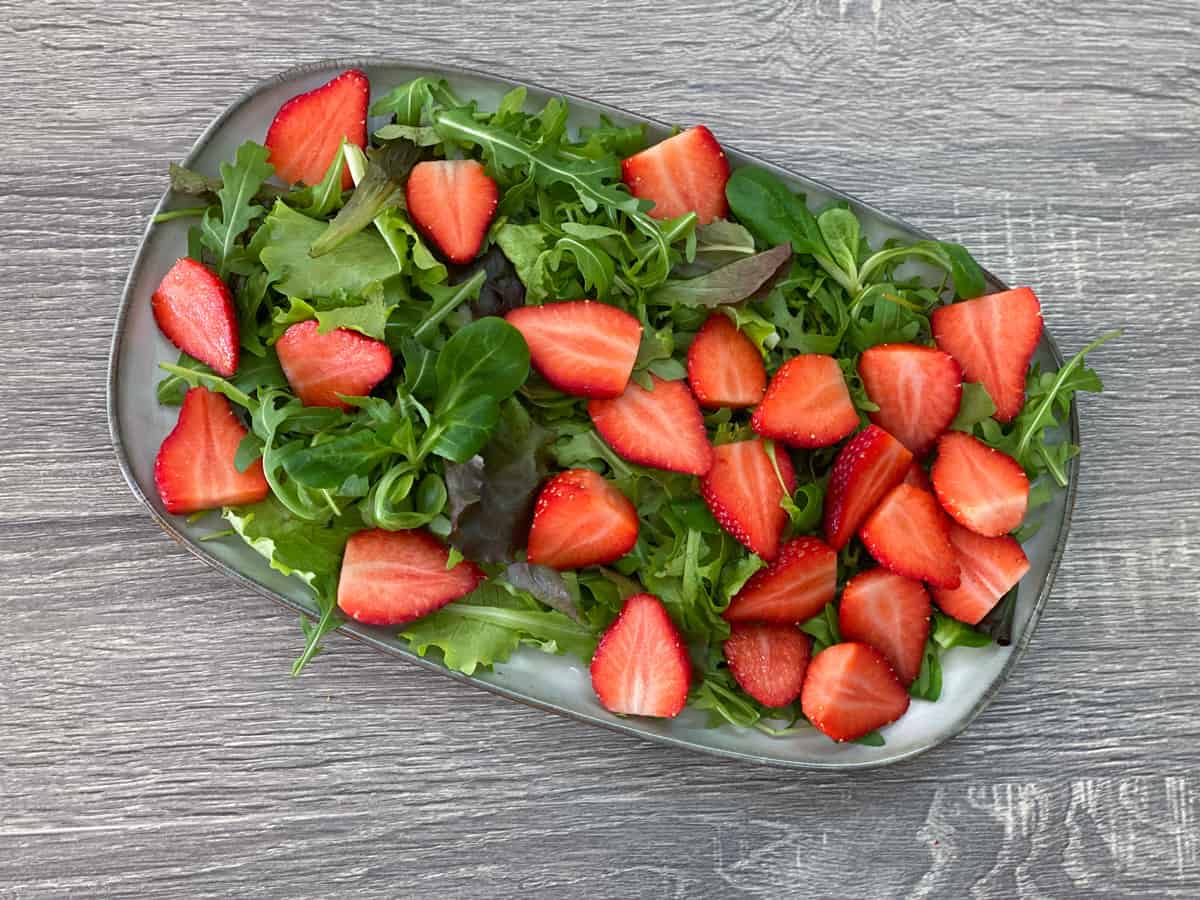 sliced strawberries added to the top of salad greens