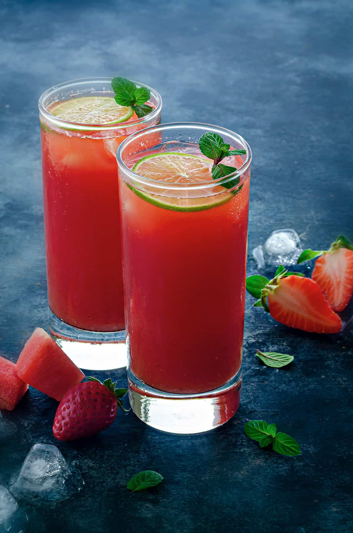 two tall glasses filled with watermelon strawberry lemonade garnished with lemon slices and mint sprigs