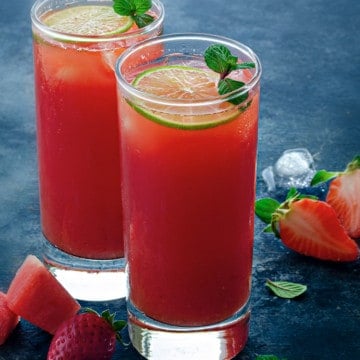 Watermelon strawberry lemonade served in two tall glasses with strawberries in the background