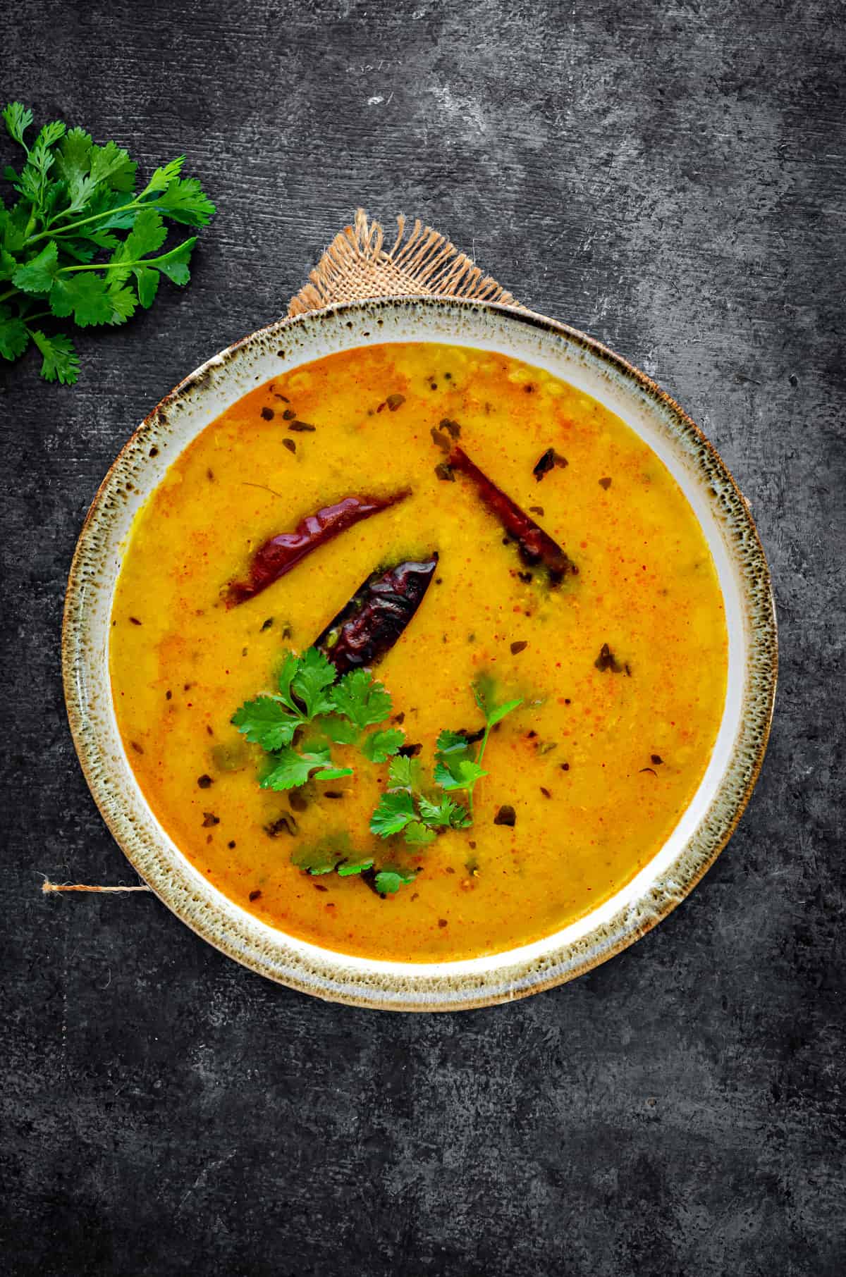 Top-down view of an earthen bowl with Rajasthani yellow dal garnished with fresh cilantro.
