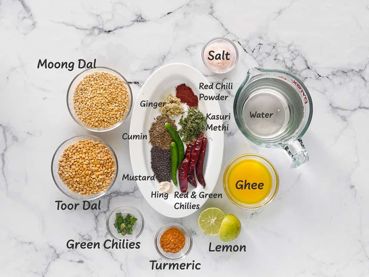 Ingredients for yellow lentils recipe in individual bowls placed in white marble platform.