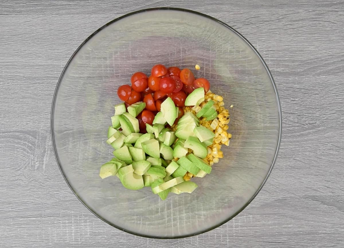 grilled corn kernels, halved cherry tomato and diced avocados in large glass bowl