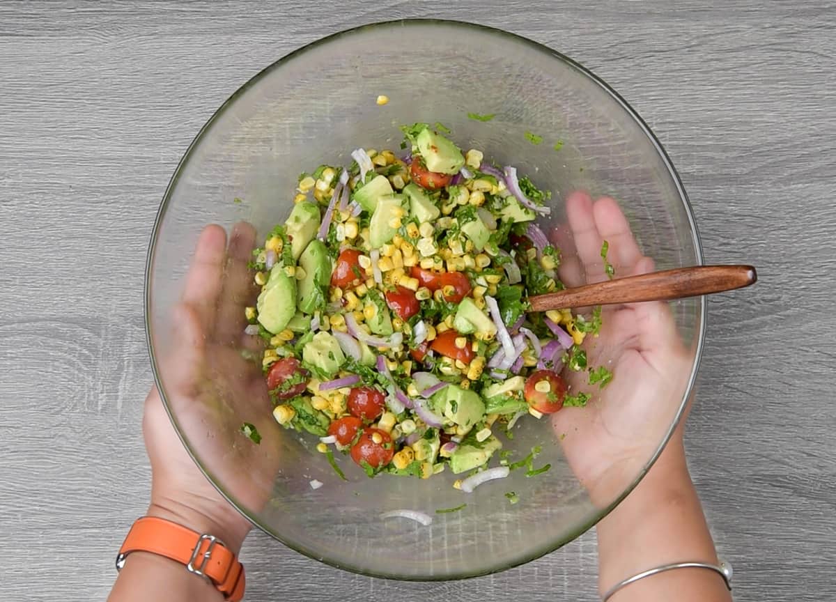 two hands holding a bowl of tomato avocado corn salad