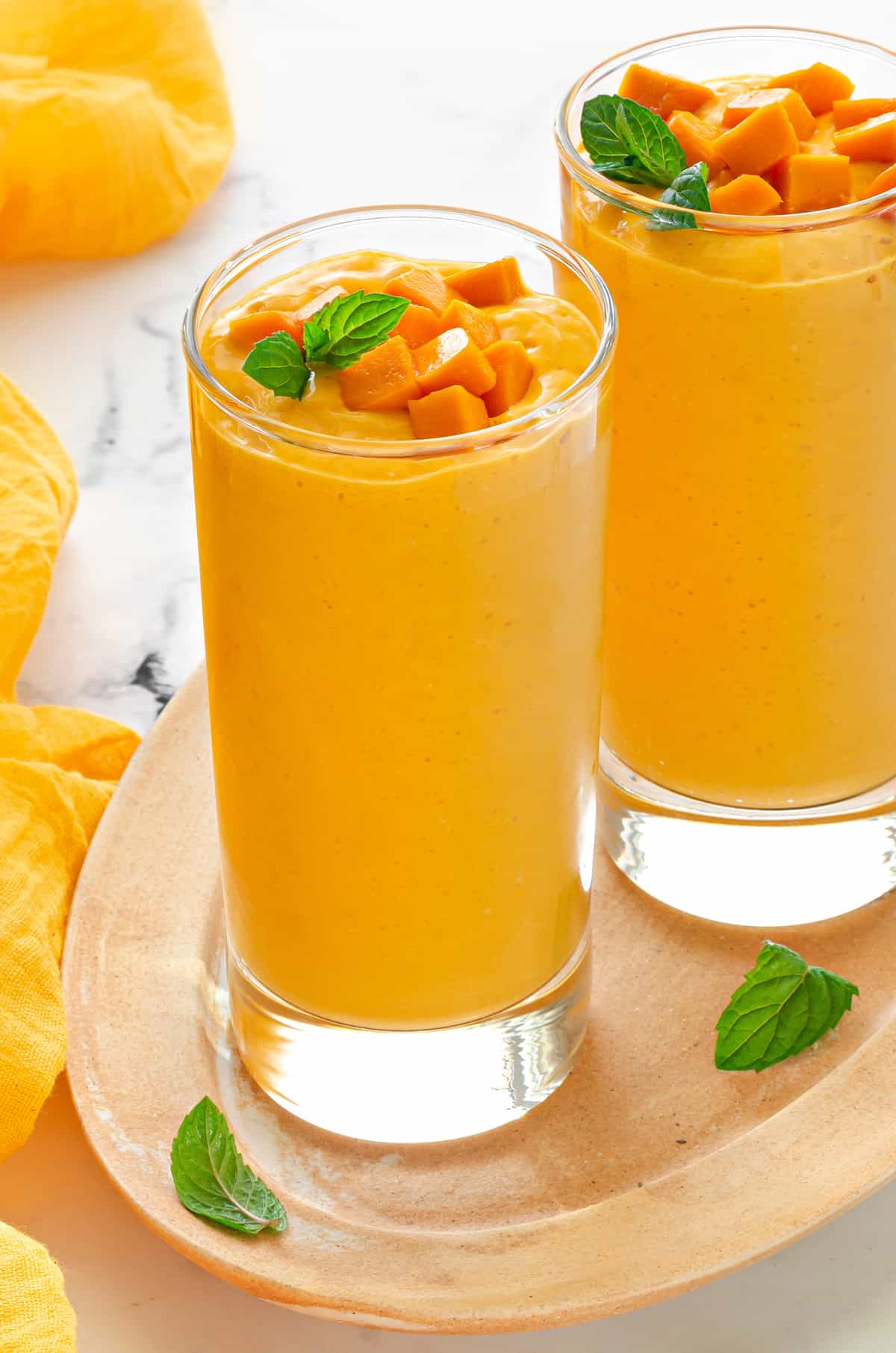 tall collins glass filled with mango oat smoothie and topped with fresh mango and mint.