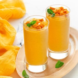 two tall collins glasses filled with yogurt mango smoothie and topped with fresh mango