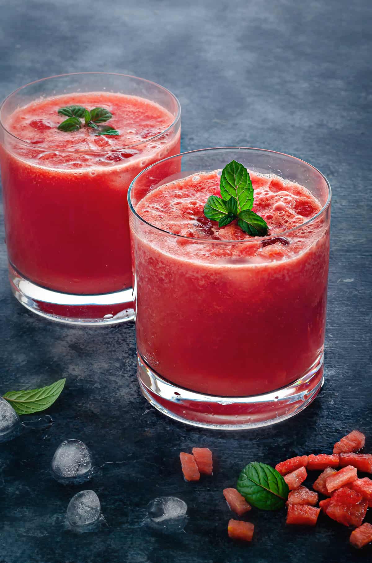 two rocks glasses of fresh watermelon juice on ice garnished with fresh mint leaves