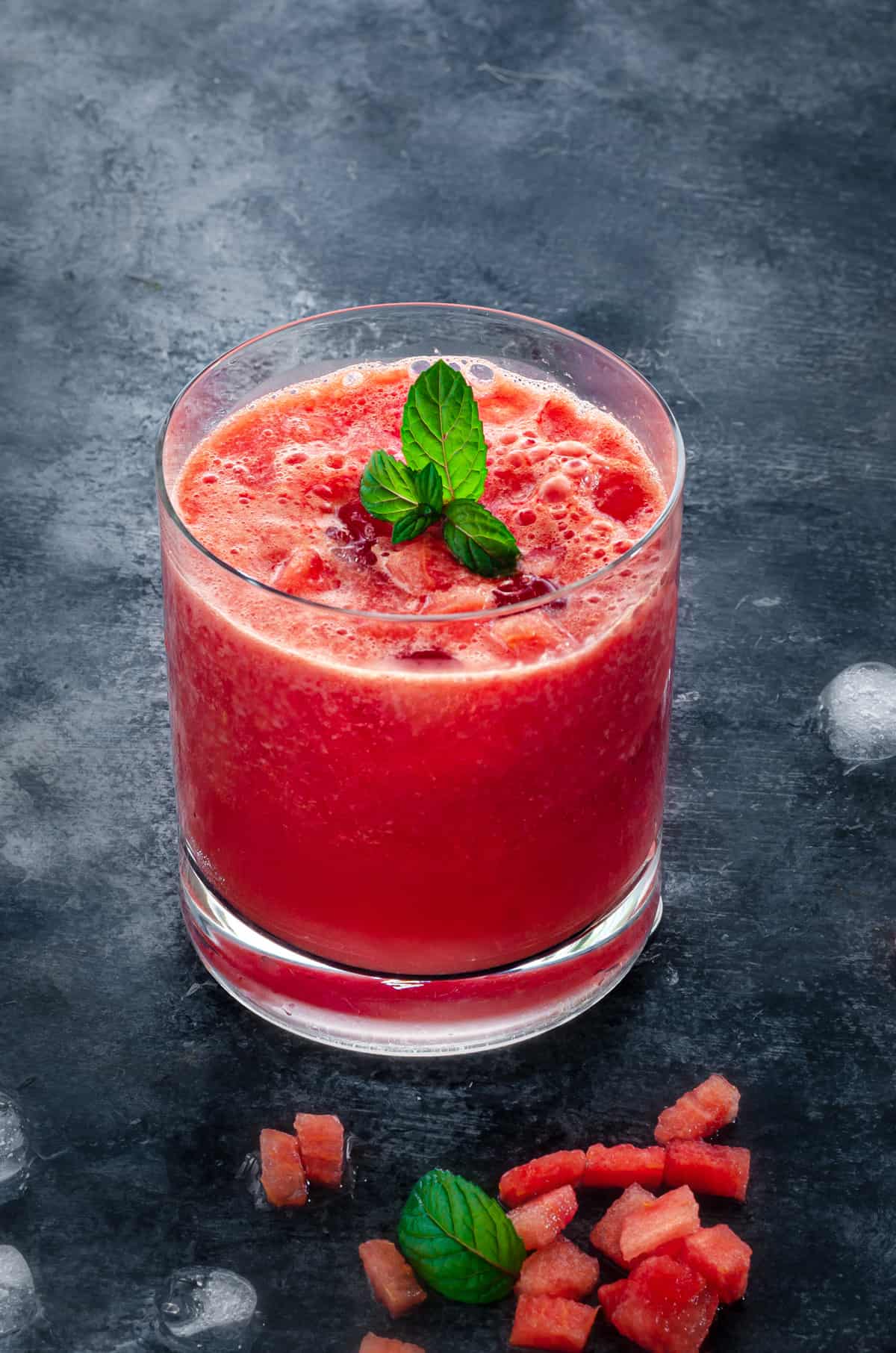 short rocks glass of watermelon juice on ice with a sprig of mint