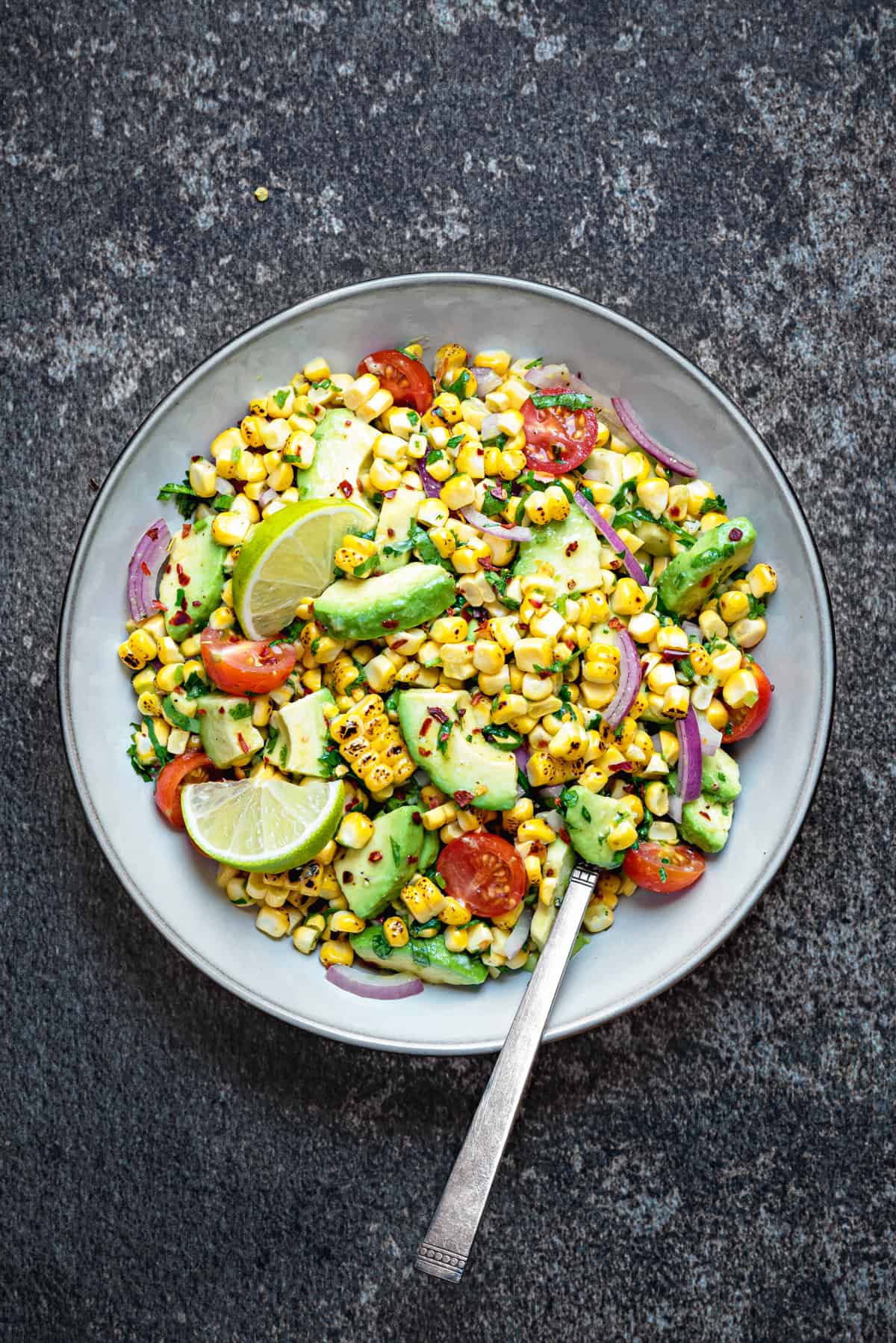 Summer corn avocado salad served in grey earthen bowl with a spoon into it