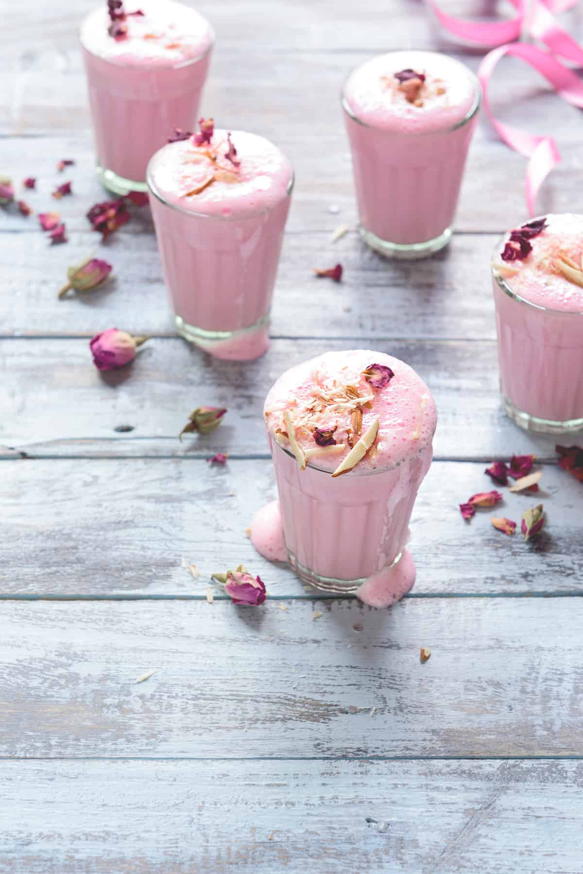 refreshing rose almond lassi in five glasses garnished with sliced almonds and dried rose petals