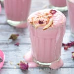 Rose lassi in glass garnished with sliced almonds and dried rose petals