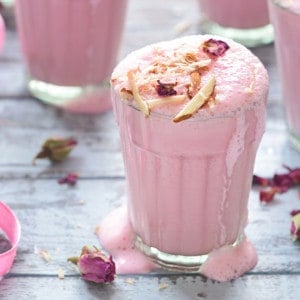 Rose lassi in glass garnished with sliced almonds and dried rose petals