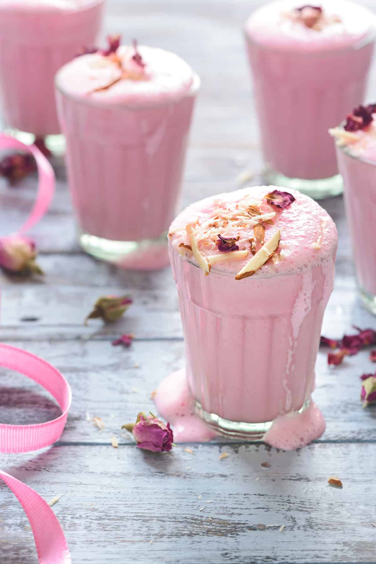 pink rose lassi in glass topped with slivered almonds and some rose buds spread around