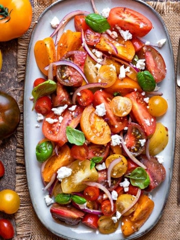 close up shot of heirloom tomato salad with feta cheese on a grey oval platter