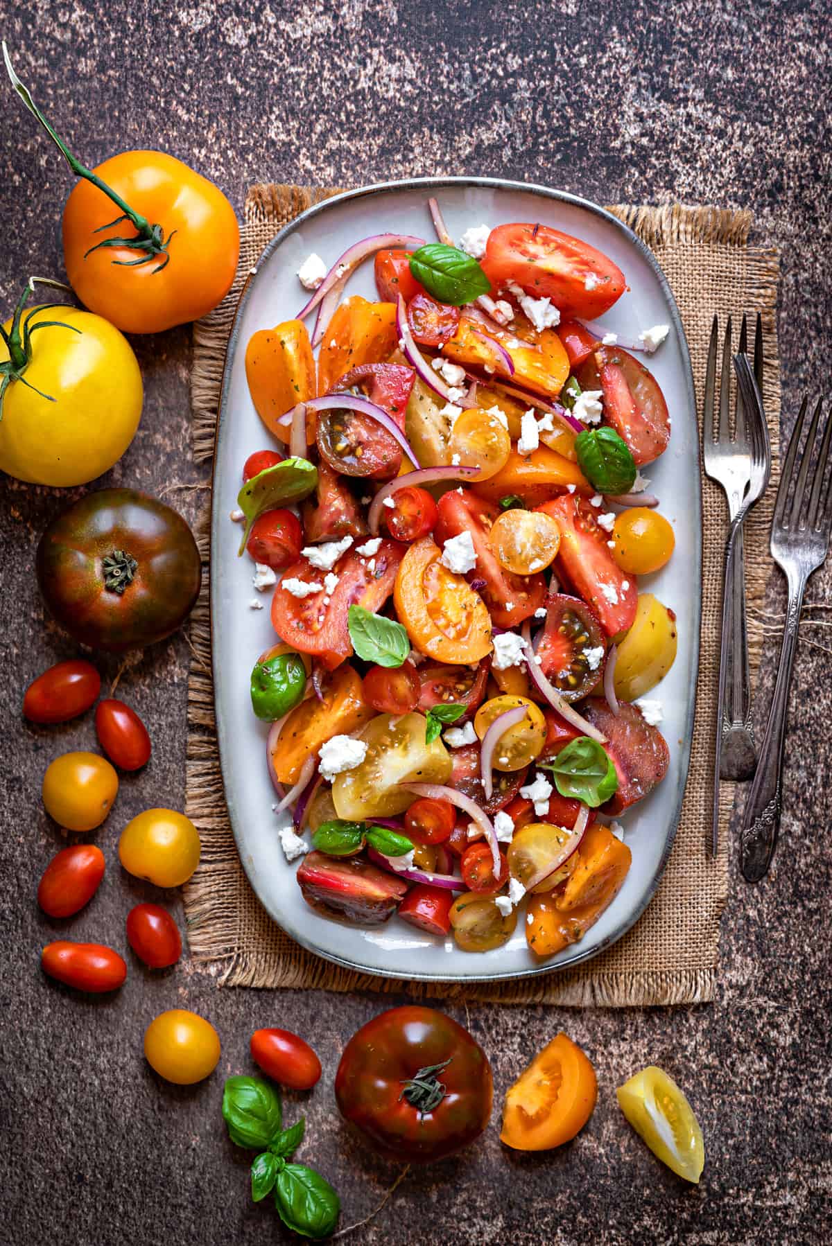 oblong serving plate with tomato feta salad on a wooden table next to whole heirloom tomatoes