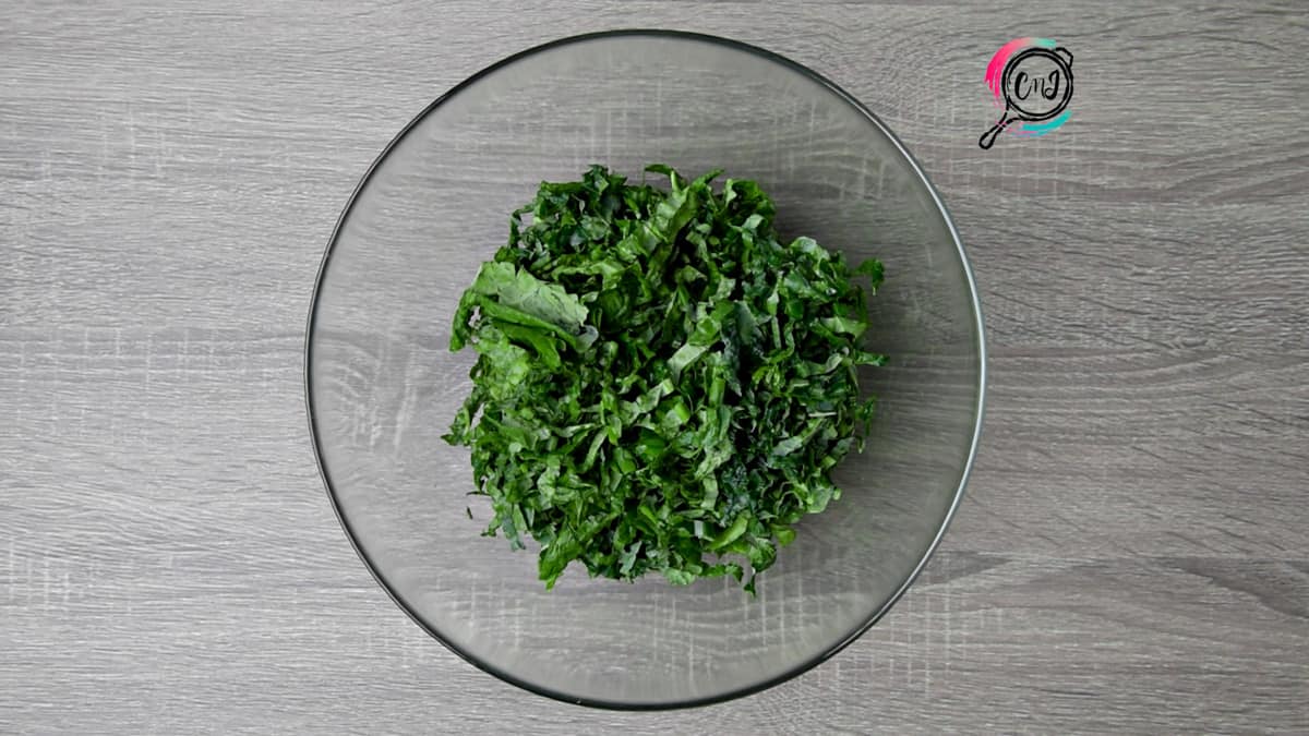 ribbons of kale in a clear glass mixing bowl on a grey table