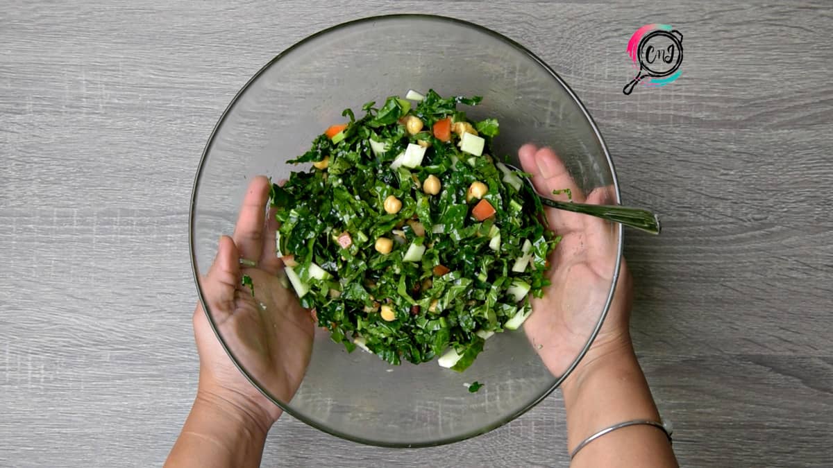 hands holding clear glass bowl of tossed kale apple salad