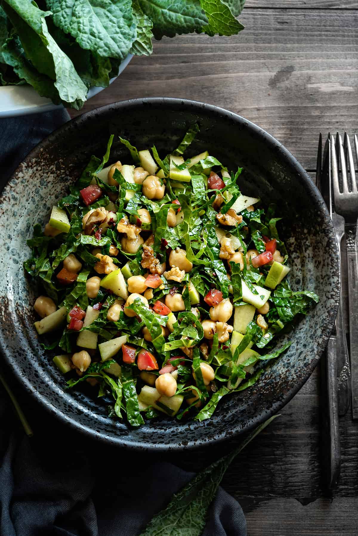 kale apple salad in a grey speckled bowl on a grey table with silverware on side