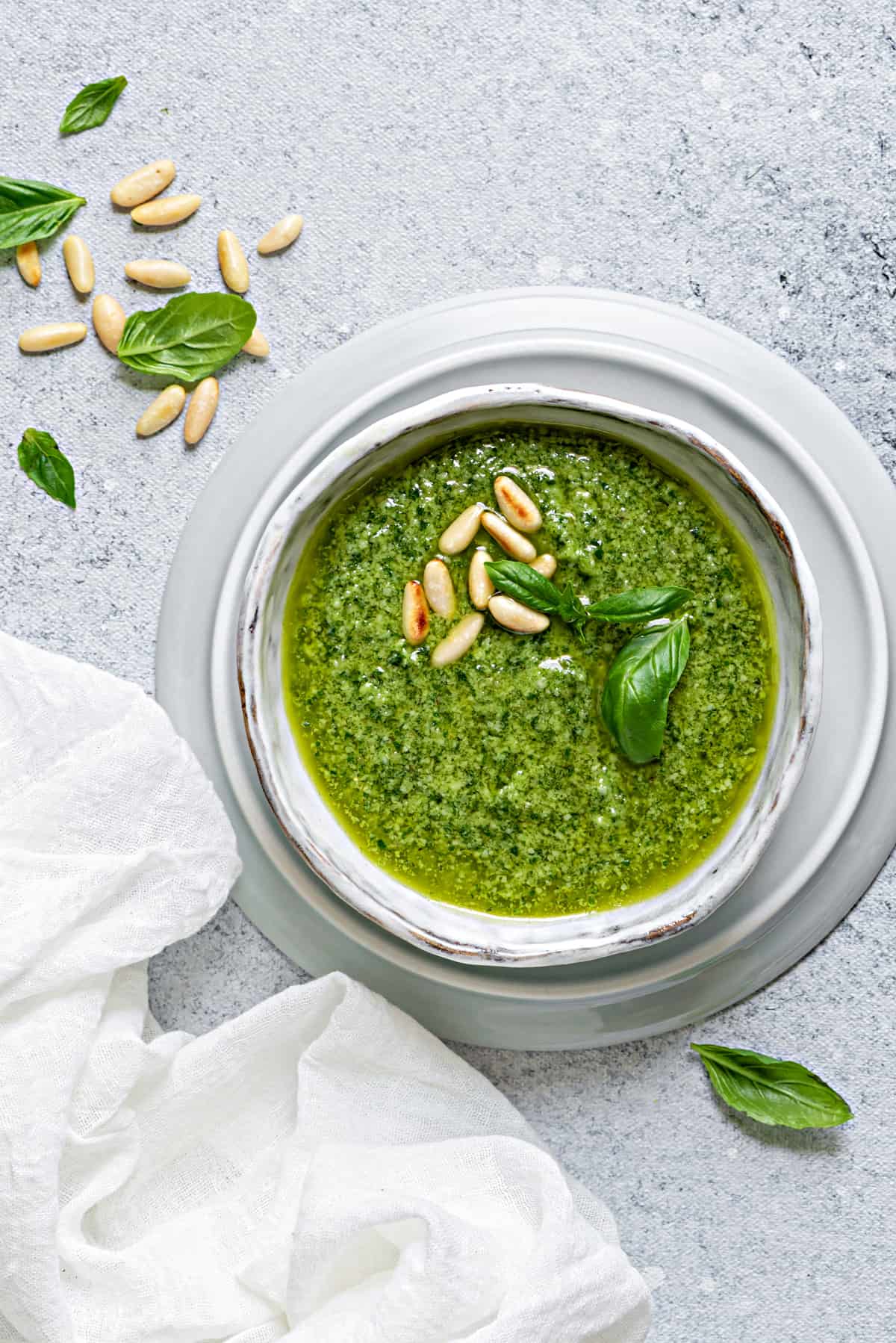 basil pesto in a serving dish on a grey table with a scattering of toasted pine nuts