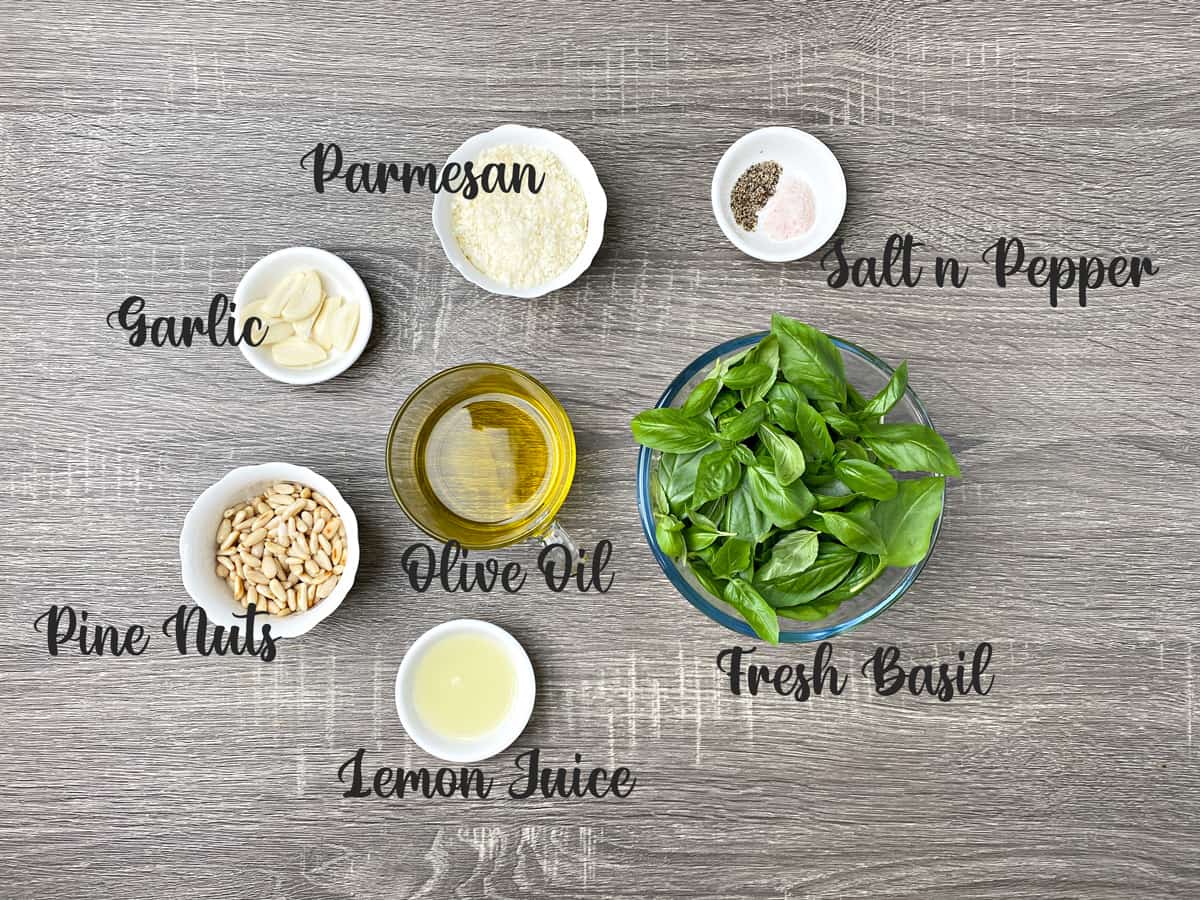 ingredients for basil pesto sauce placed in glass bowls and kept on a grey wooden table