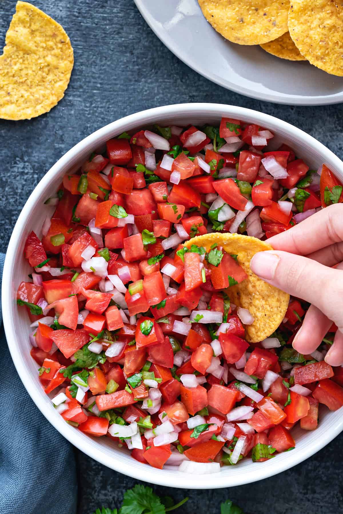 hand dipping a round tortilla chip into a white bowl of pico de gallo salsa fresca