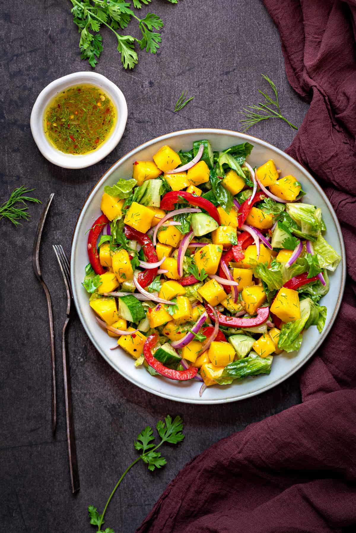 mango salad in a grey bowl with two forks and dressing in bowl kept on side