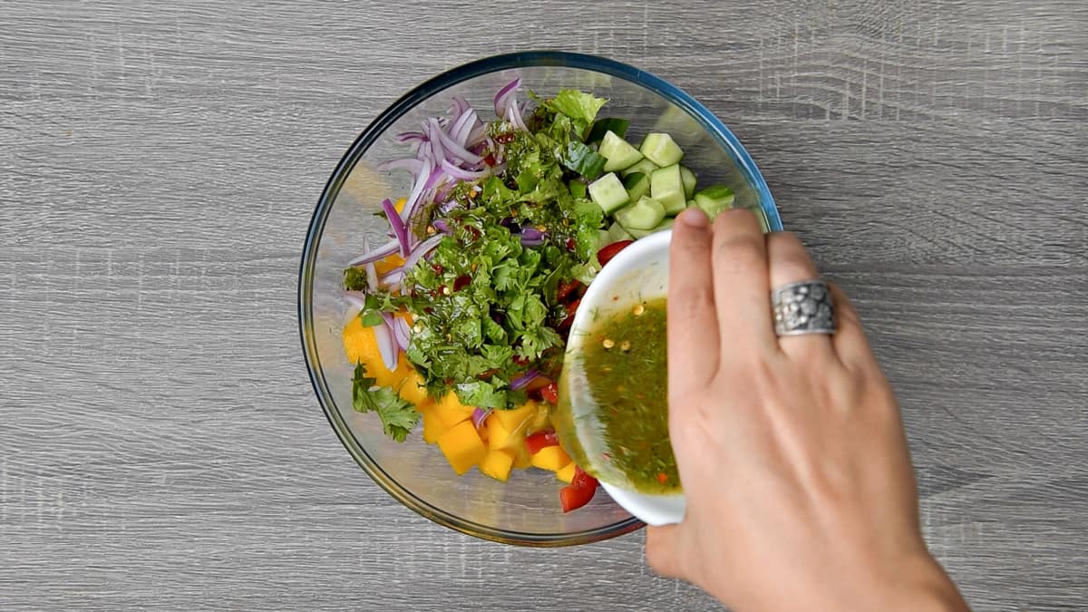 salad dressing being poured over veggies and mango