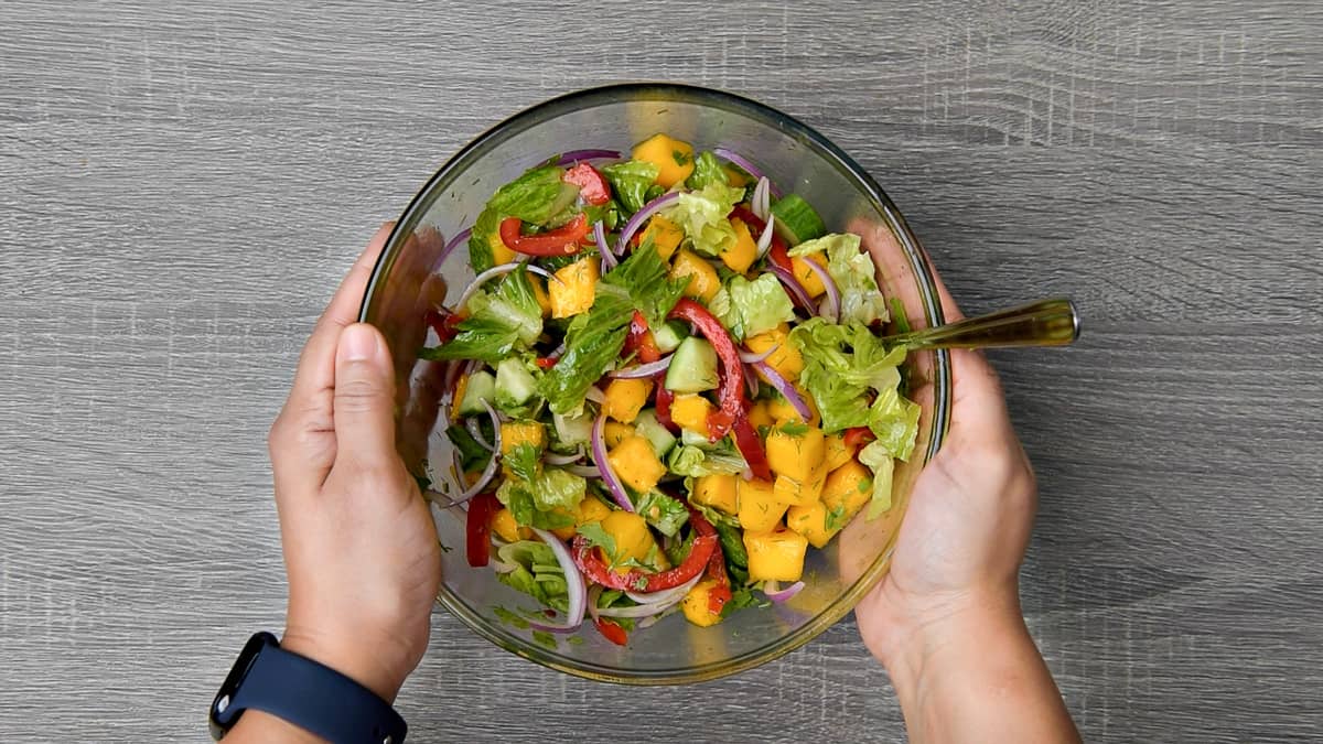 hands holding completed bowl of mixed mango salad