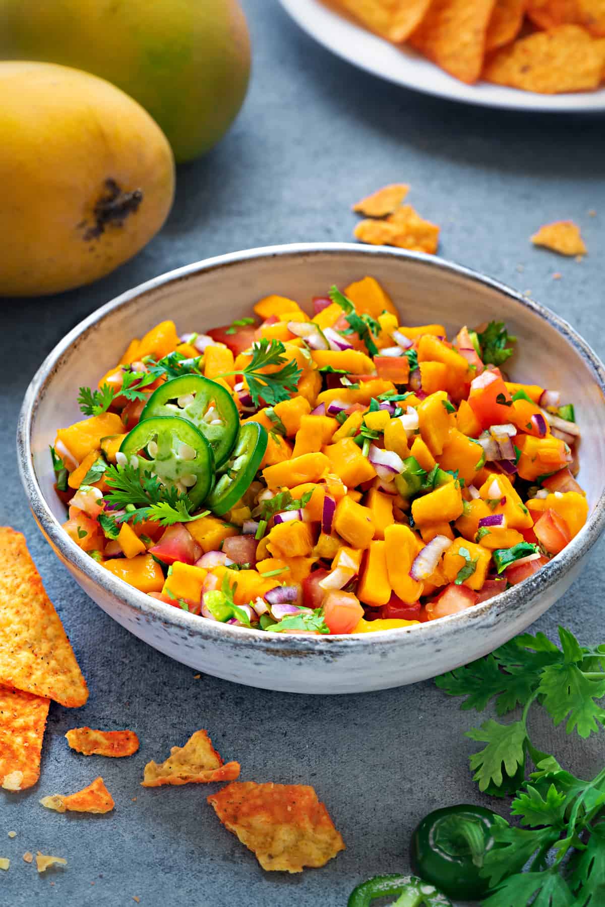 mango salsa in a white earthenware bowl next to a plate of tortilla chips and mangoes