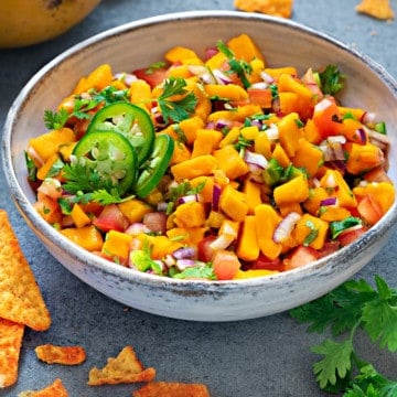 mango salsa in a white earthenware bowl next to a plate of tortilla chips and mangoes