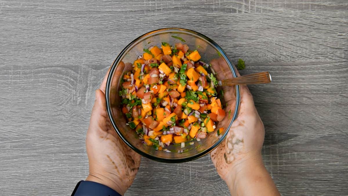 hands holding bowl of mango salsa after tossing ingredients together