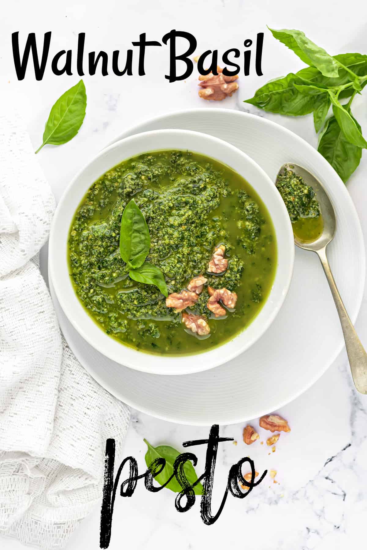 walnut basil pesto in white bowl with a spoon on side placed on a white table