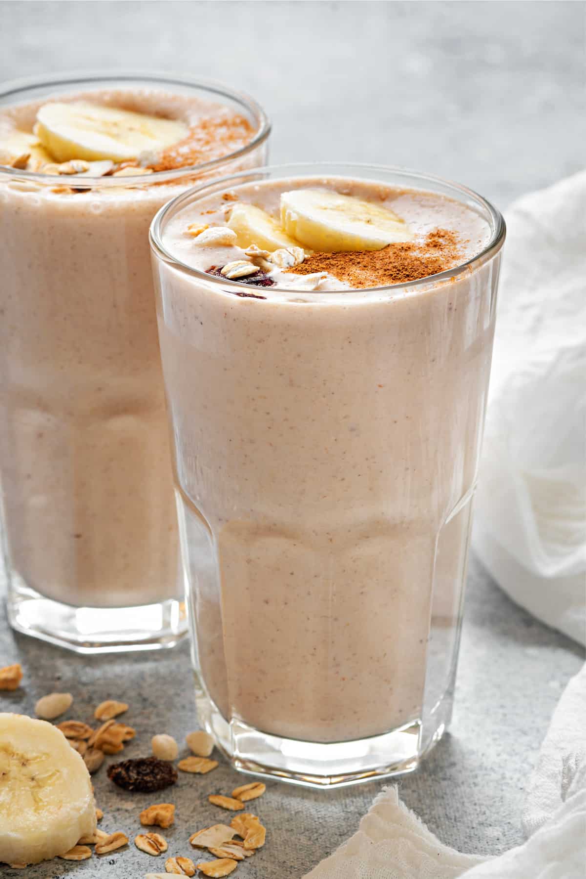 Two tall clear glasses filled with healthy banana breakfast smoothie mix and topped with cinnamon