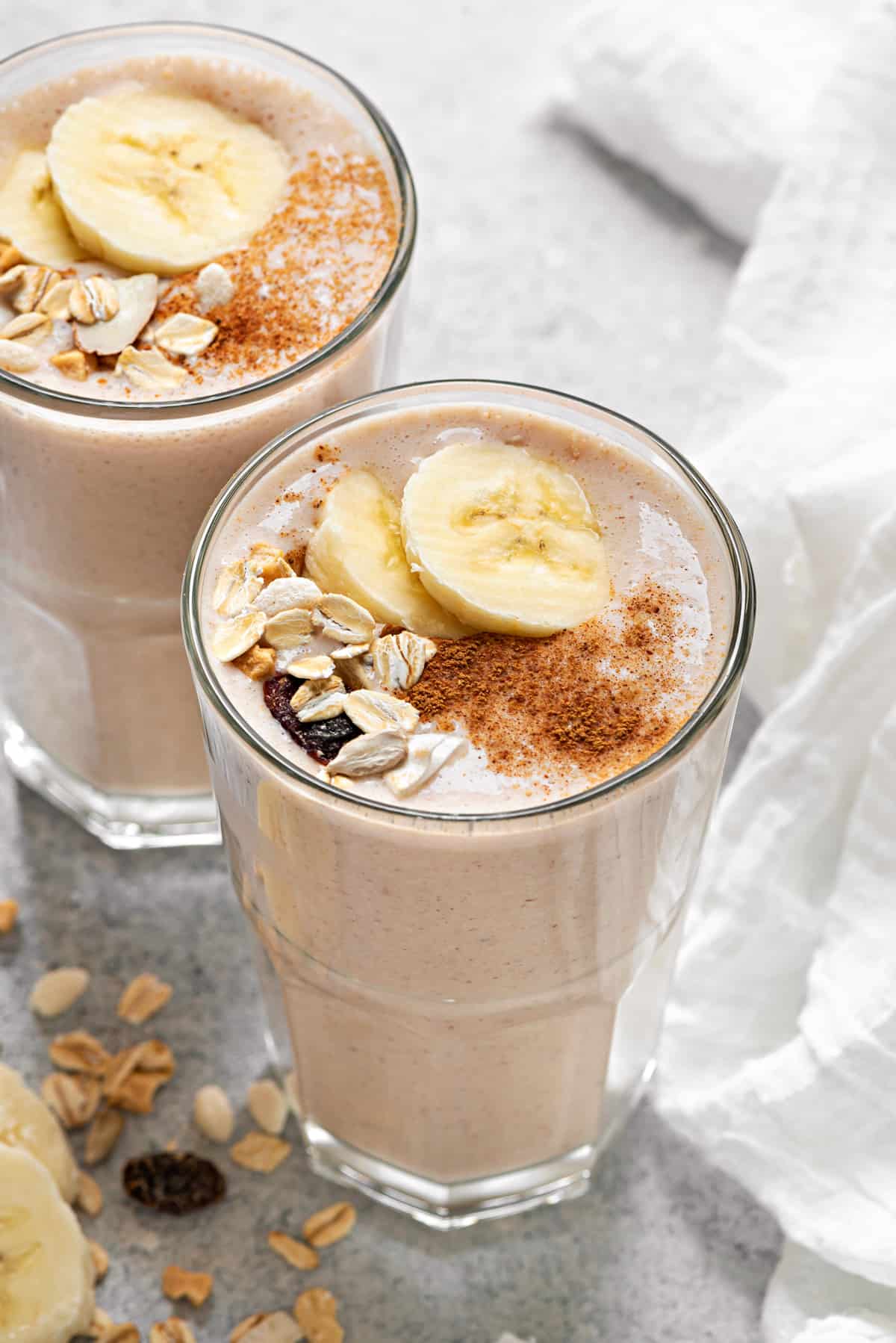 healthy banana breakfast smoothies topped with sliced banana, muesli and dusted with cinnamon