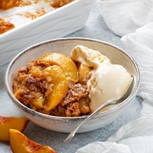 white bowl with a serving on peach cobbler and vanilla ice cream kept on a table