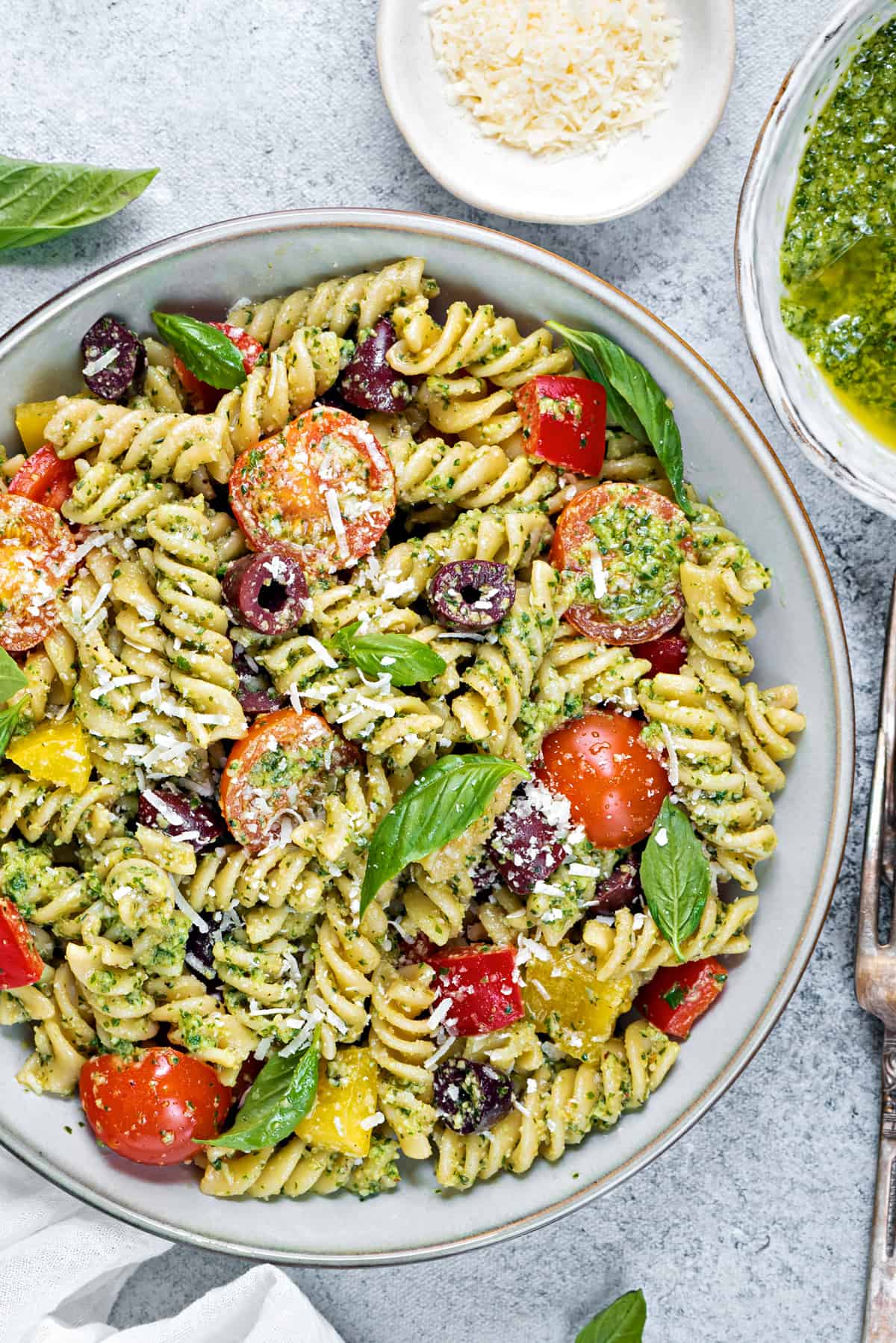 close up of a bowl of pesto pasta salad garnished with fresh basil and grated parmesan 