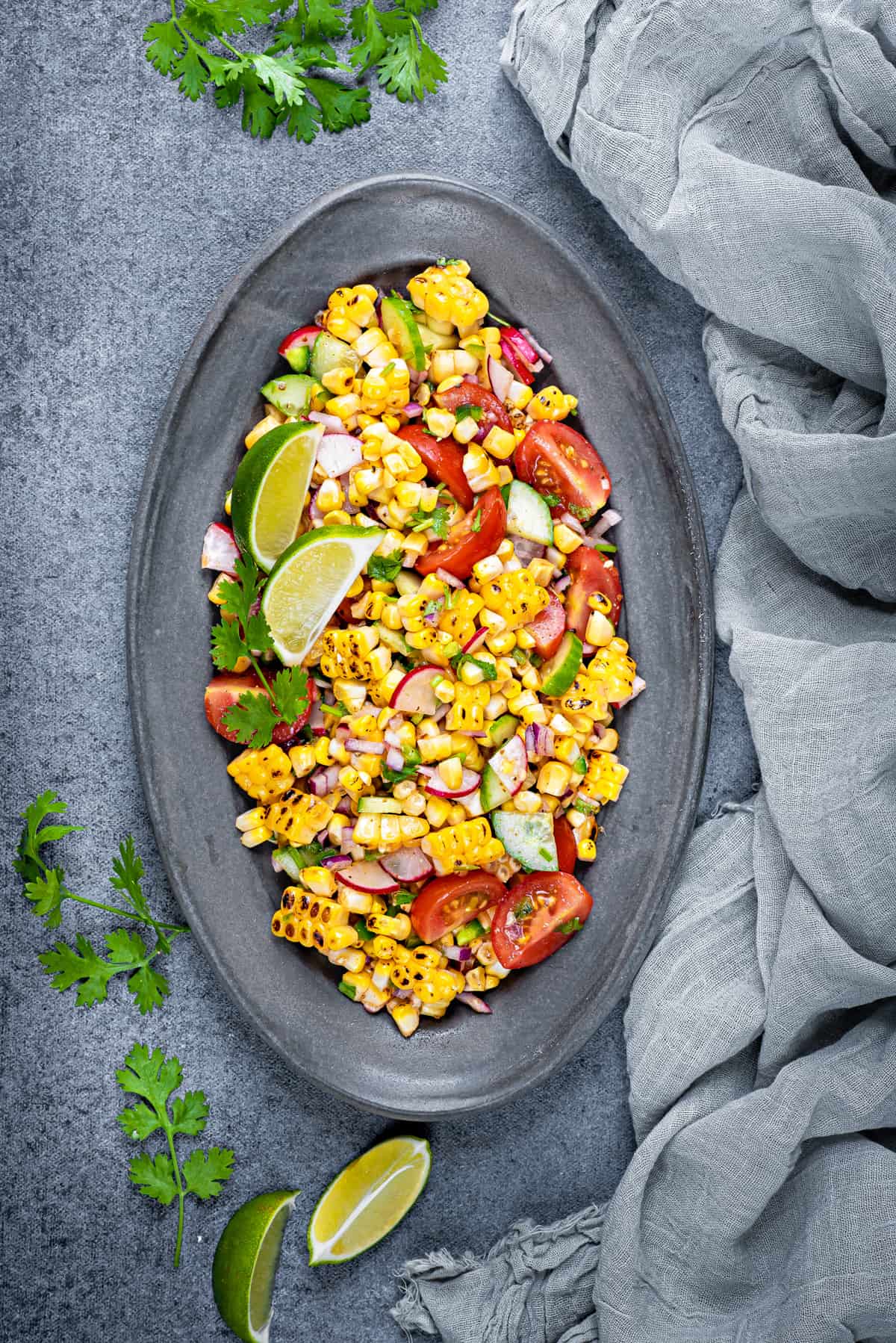 overhead shot of serving platter of corn salad on a grey table with a grey cloth