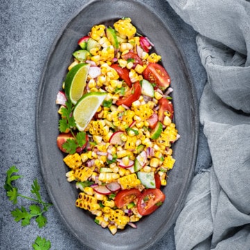 Serving plate loaded up with fresh summer corn salad garnished with lime wedges and fresh cilantro