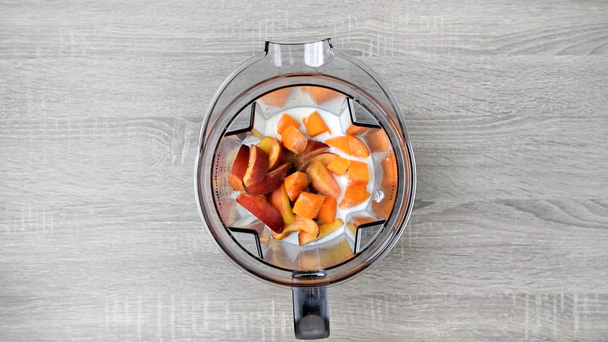 overhead shot of peach smoothie ingredients in a blender pitcher