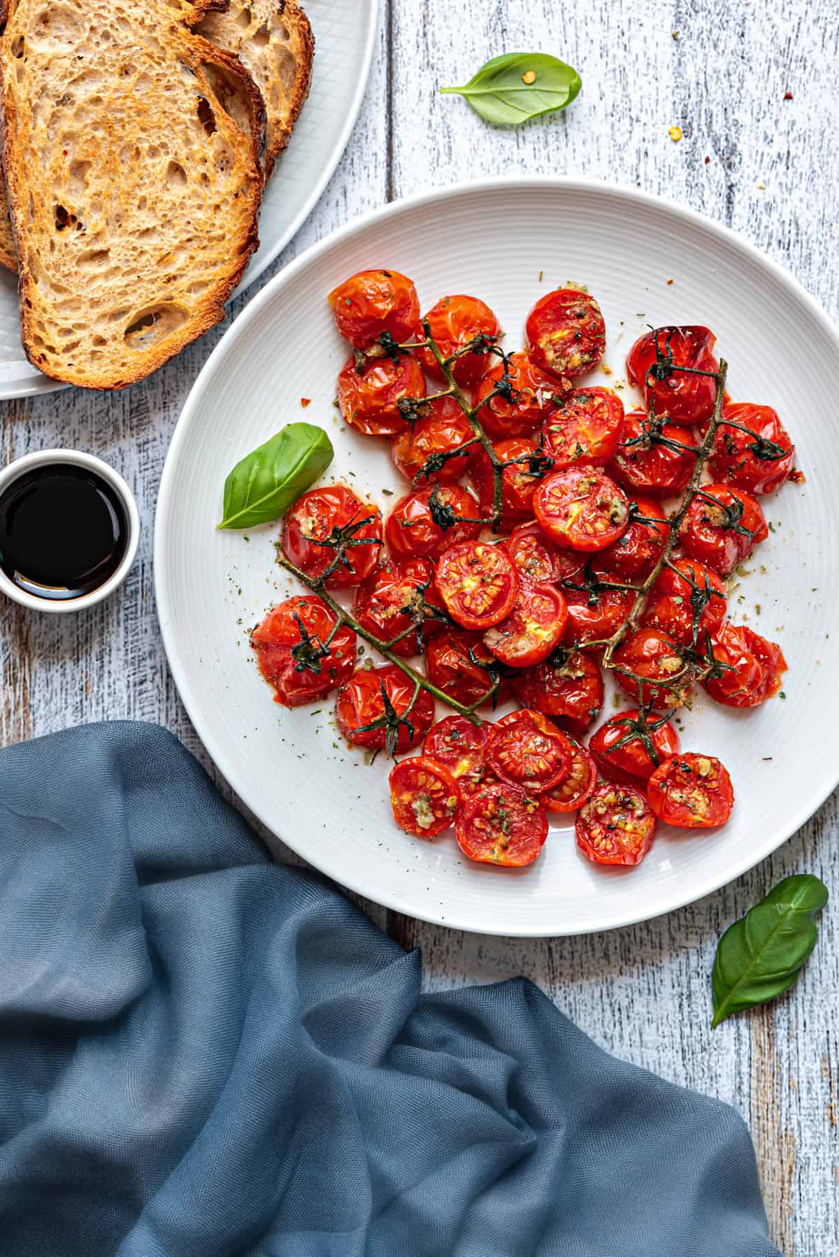 a pile of oven roasted tomatoes on a white plate next to toasted bread slice