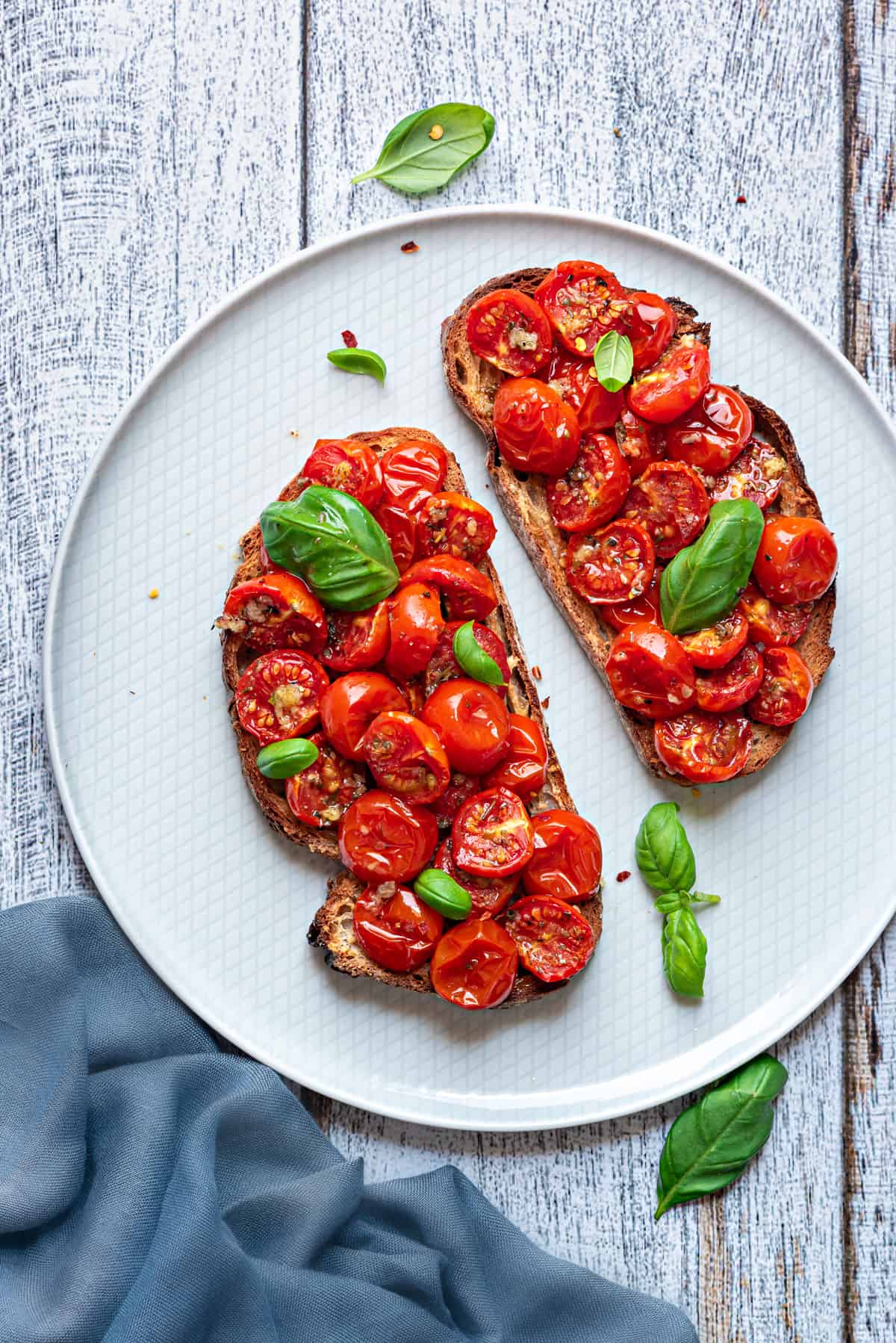 roasted cherry tomatoes on two pieces of toast and garnished with fresh basil leaves