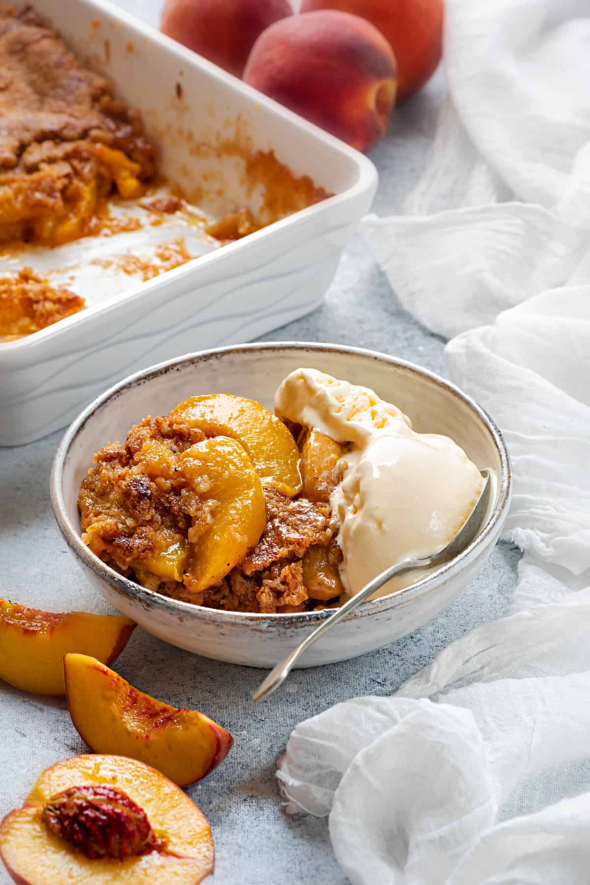 white bowl with a serving on peach cobbler and vanilla ice cream kept on a table