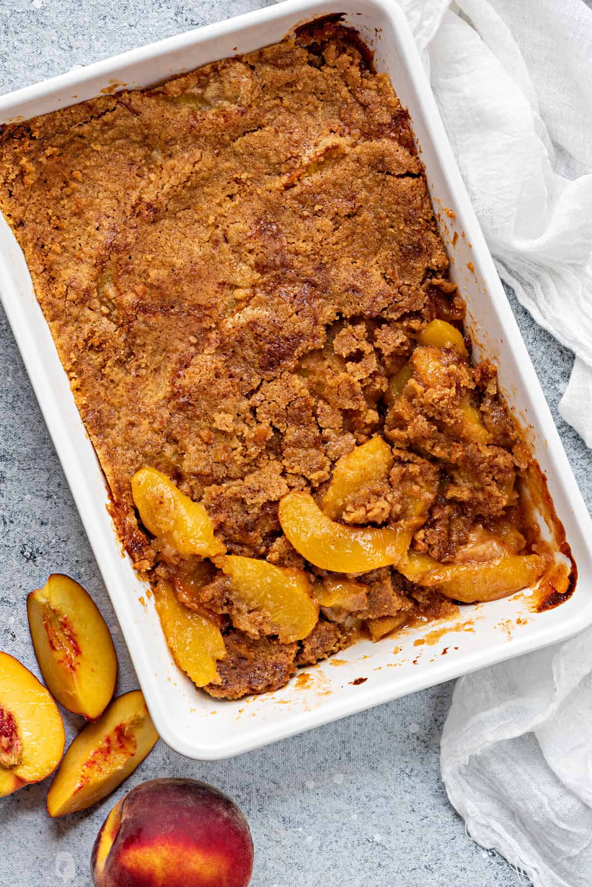 flat lay shot of white casserole dish of baked homemade peach cobbler on a grey table