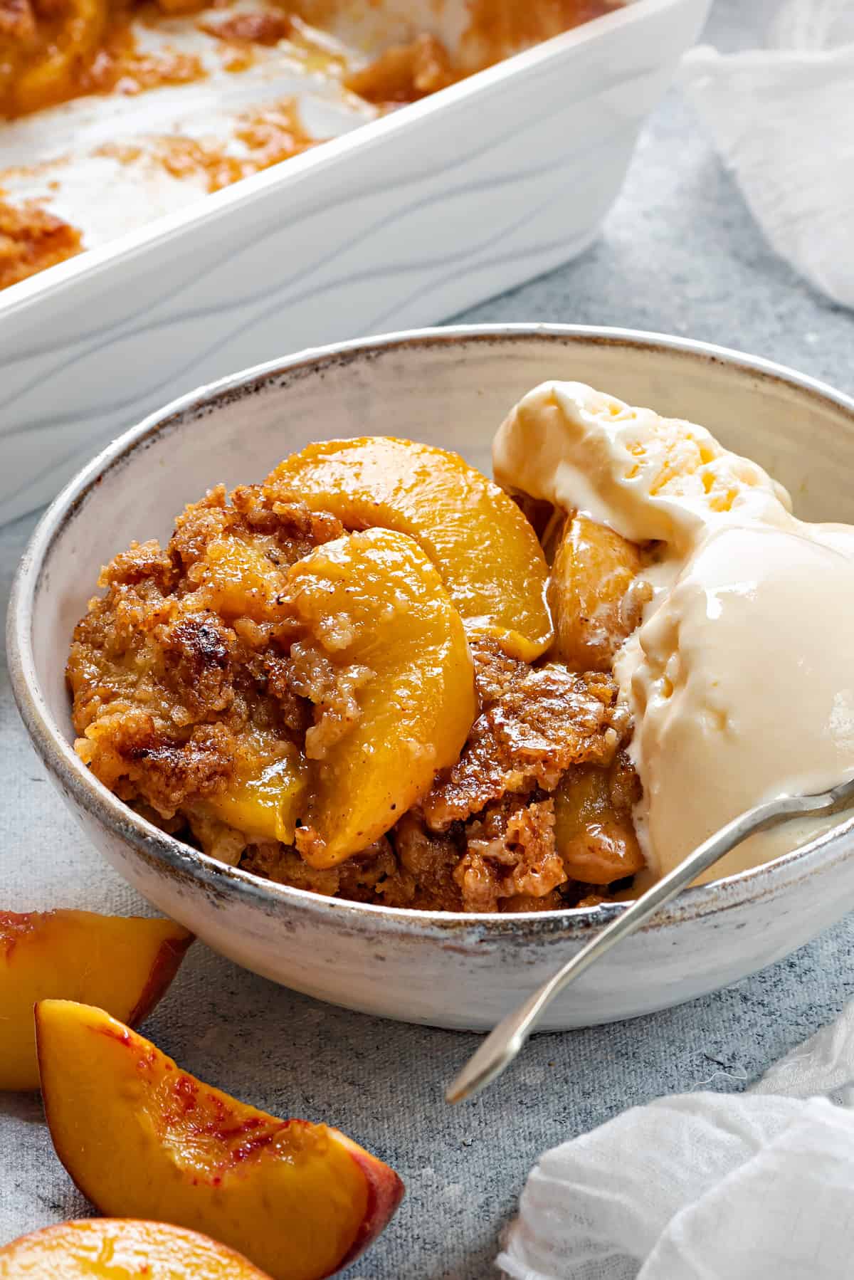 close up shot of peach cobbler in a bowl with ice cream, highlighting the texture of the juicy peaches and the crispy topping 