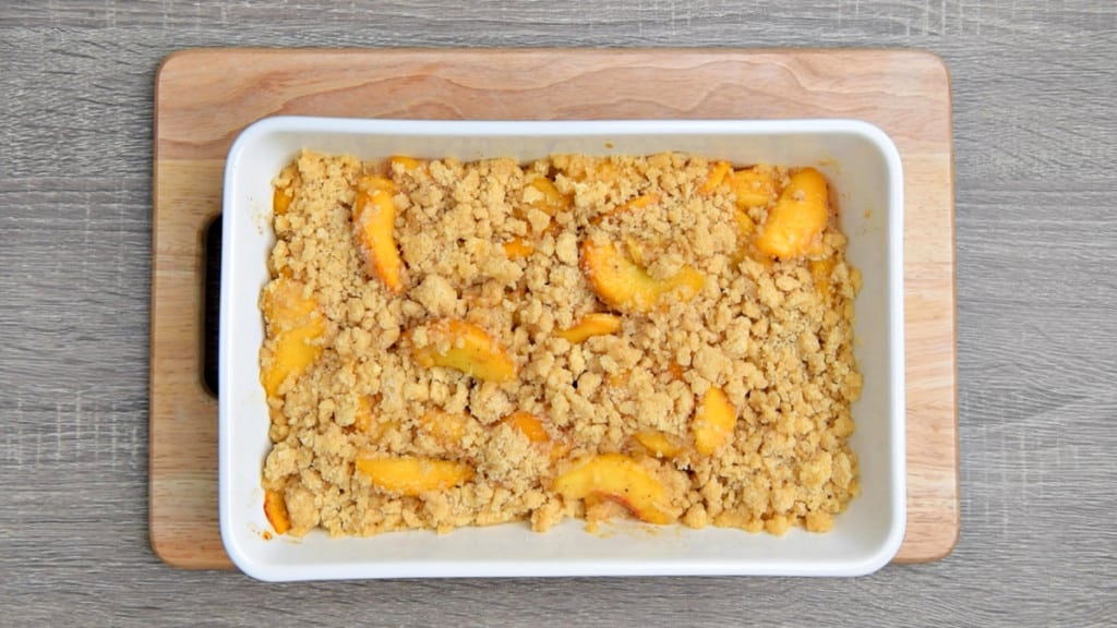 raw cobbler filling sprinkled over par-baked peaches