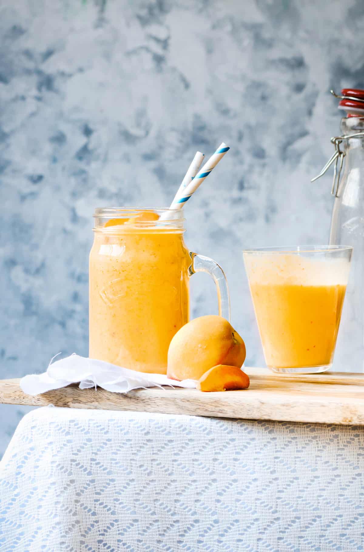 clear glass filled with mango peach smoothie and garnished with a blue and white paper straw