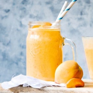 mango peach smoothie in a glass on a wooden board with a fresh peach in the foreground